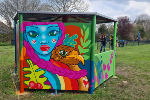 Photo of rain shelter for teenagers with brightly coloured decorative "graffiti" showing a blue face and a bird